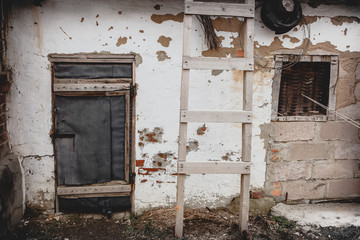 Old white wall of a house with peeling paint and an old closed door. Decrepit building.