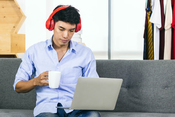 Young Asian man working on laptop while drinking coffee and listening to music.