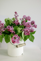 Bouquet of pink lilac in a white metal can on a light background. 