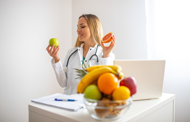 Female nutritionist with fruits working at her desk. Smiling nutritionist in her office, she is...