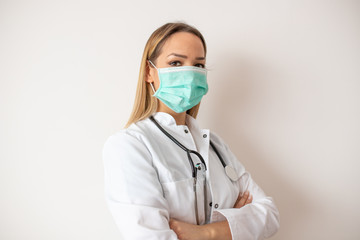 Confident doctor standing arms crossed. Confident young woman doctor. Intern Doctor Young pretty woman in white clothes with medical mask posing.