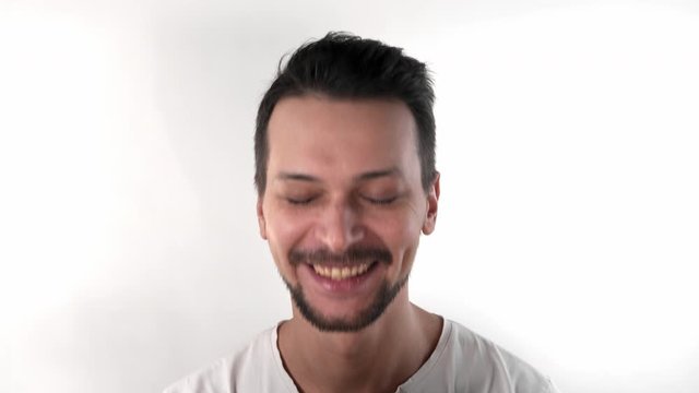 Caucasian brunette man with short hair with a beard in the studio on a white background in a white T-shirt smiles and laughs and throws his head back, close-up