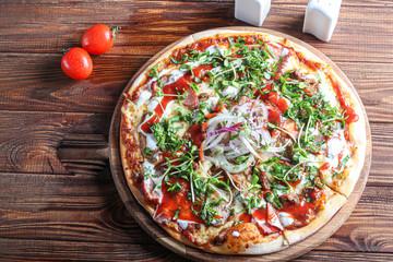 Pizza with bacon and herbs on a wooden plate with cheese and tomato sauce. On a dark background.