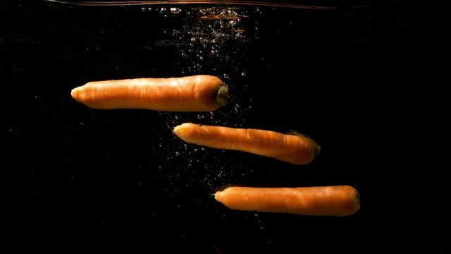 Three Carrots Dump Into The Water And Slowly Sink Into The Deep. -medium shot