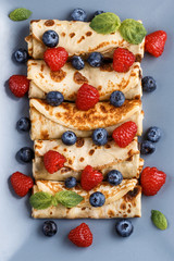 Twisted thin pancakes with raspberries and blueberries decorated with mint. Food on a gray square plate. Russian kitchen. Close-up.