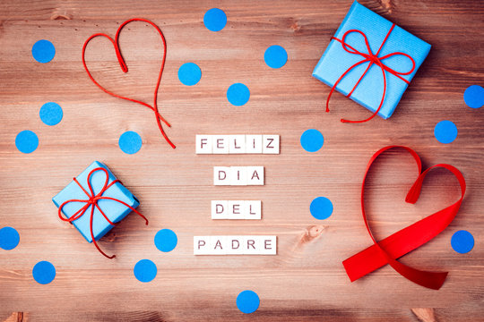 Feliz dia del padre words made of wooden blocks with blue gift boxes and red hearts on wooden background. Happy fathers day greeting card, holiday flat lay, top view