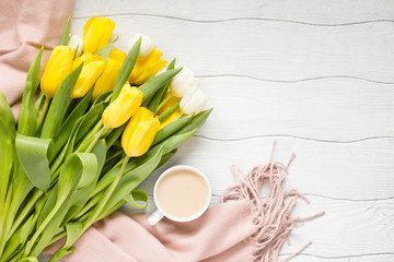 Spring composition a bouquet of yellow tulips and a Cup of coffee with a woman's scarf of powdery color on a white wooden table
