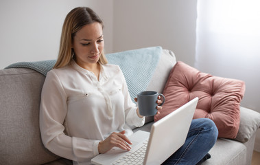 Woman using laptop on a home couch. Woman surfing on line or working from home concept