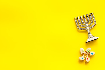 Jewish holiday Hanukkah with menorah - traditional Candelabra - and wooden dreidels spinning top. Yellow background, top view, copy space
