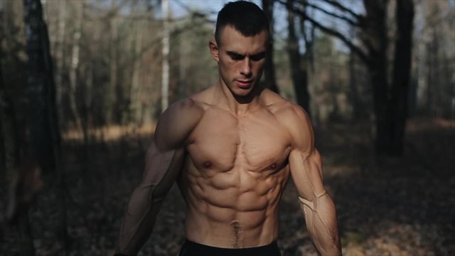 Big muscular male athlete in the forest shows muscles topless and running. Slow motion