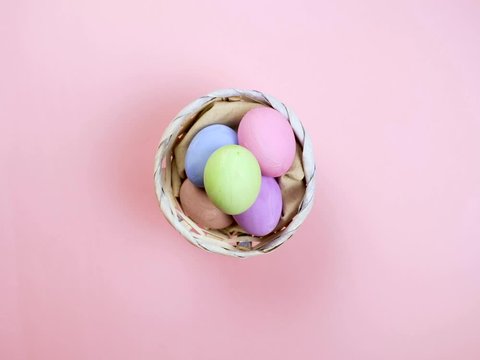 Happy Easter holiday concept stop motion animation. Colorful egg appear on right side and put into basket, pink background. Space for creative and design, copyspace, top view