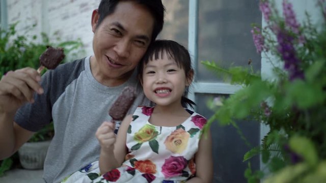 Little asian girl and father eating ice cream together happily. Father and daughter's happy moments. Kid and dad look at camera and smiling. Happy family concept. Handheld shot and Real life.