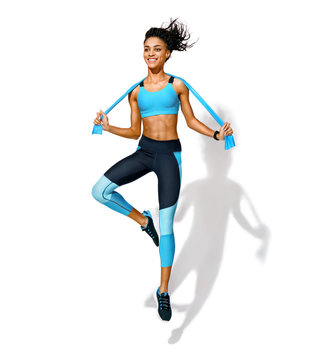 Sporty girl with elastic resistance band in motion. Photo of african american girl in fashionable sportswear on white background. Dynamic movement. Full length. Sports and healthy lifestyle
