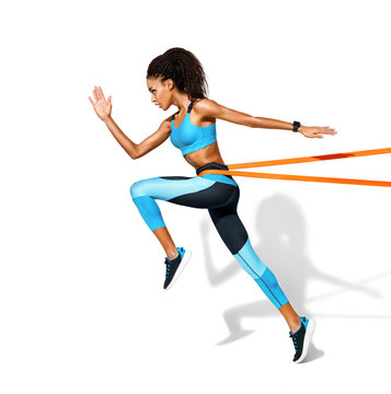 Strong girl in silhouette using a resistance band. Photo of african american girl in fashionable sportswear on white background. Dynamic movement. Side view. Full length. Sports and healthy lifestyle