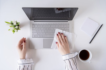 A woman worker cleaning with antivirus wet wipe a laptop and a working office desk before starting work for protect herself from bacteria and virus.