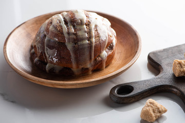 fresh homemade cinnamon roll on plate on marble surface with cutting board with brown sugar