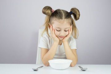 little girl holds a fork and spoon in front of a plate of eggs