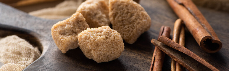 close up view of fresh cinnamon sticks and brown sugar on wooden cutting board, panoramic shot