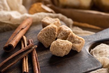 close up view of fresh cinnamon sticks and brown sugar on wooden cutting board