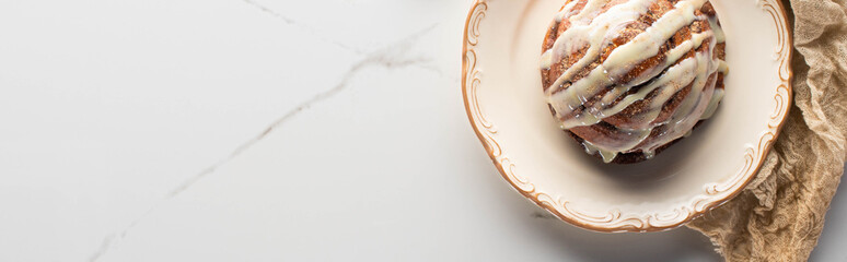 top view of fresh homemade cinnamon roll on plate on marble surface with cloth, panoramic shot