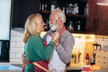 Beautiful senior couple is dancing and smiling while cooking together in kitchen. Quarantine. Health concept.