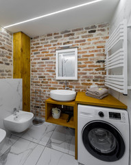 Modern bathroom in apartment. Loft interior. Brick wall. Sink and bidet. Washing machine.