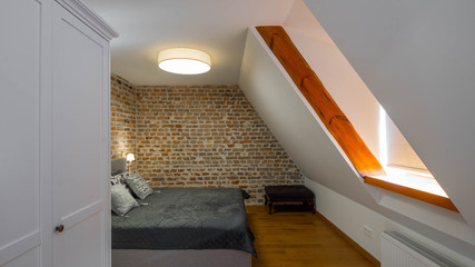 Modern contemporary loft interior of bedroom. Brick walls and sloping ceiling. Cozy bed.
