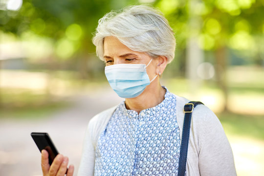 health, safety and pandemic concept - happy senior woman woman wearing medical mask for protection from virus with smartphone at summer park - Powered by Adobe