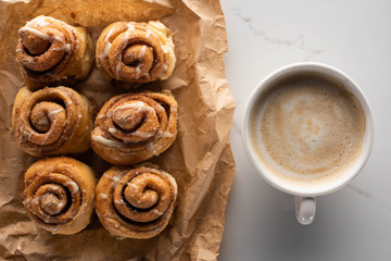 top view of fresh homemade cinnamon rolls on parchment paper on marble surface with coffee