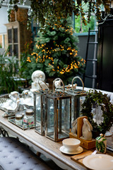 modern glass laterns with other decor on wooden table with christmas lights in the back.