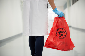 A woman worker hand holding red bag with bioharzard sign in the hospital.