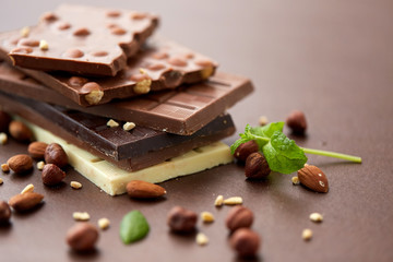 sweets, confectionery and food concept - bars of dark, white and milk chocolate with nuts on brown background