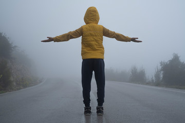 A facing back hoody boy raised hands on both sides, standing in an abondoned road in air pollution,...