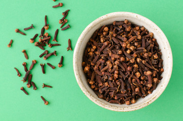 Cloves in bowl on green background. Top view. Cloves spice.