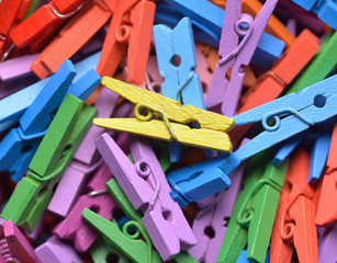 Multicoloured painted wooden mini clothes pegs in random pile. Top down macro photo with selective focus on central yellow peg.