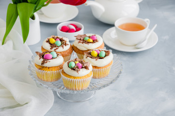 Homemade Easter vanilla cupcakes bird's nest with butter cream, chocolate and candy eggs on a dish. Easter fun food idea for kids. Horizontal orientation. Copy space.