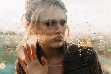 Fototapeta na wymiar girl model looks through the glass covered with raindrops