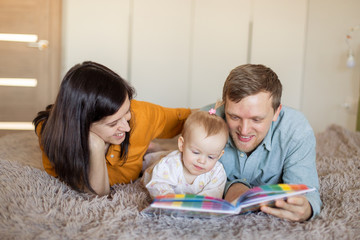 happy young family spends time together. Mom and Dad are reading a book to a child. literature early development of the baby. parenting. Modern parents are millennials. Learning in game activities 