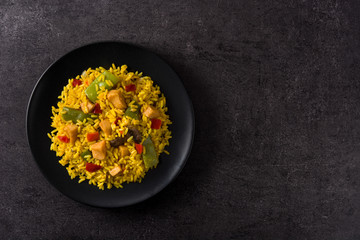 Fried rice with chicken and vegetables on black plate and black background. Top view copy space