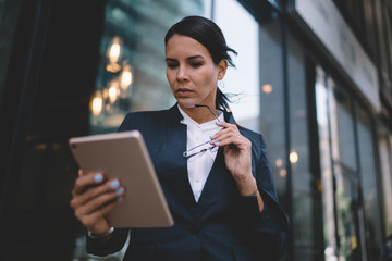 Thoughtful businesswoman reading information on tablet in urban street