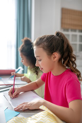 Two girls of the same age drawing at the table.