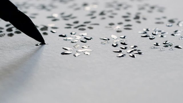 Macro shot of a black paint brush drawing ink patterns on an off-white paper, in front of more ink-drawn patterns