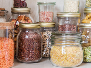 Shelf in the kitchen with various cereals and seeds - peas split, sunflower and pumpkin seeds, beans, rice, pasta, oatmeal, couscous, lentils, bulgur in glass jars