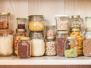 Shelf in the kitchen with various cereals and seeds - peas split, sunflower and pumpkin seeds, beans, rice, pasta, oatmeal, couscous, lentils, bulgur in glass jars