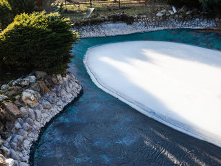 Large pond in the garden with frozen water. Home-made pond and ice inside it in winter
