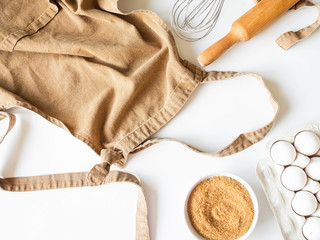 Ocher apron and various baking ingredients - eggs, sugar and kitchen utensils on white background....