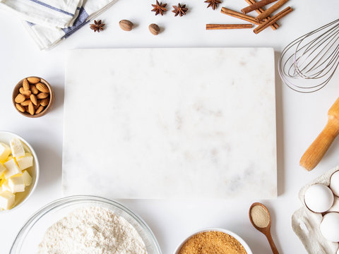 Frame of various baking ingredients - flour, eggs, sugar, butter, dry yeast, nuts and nuts, kitchen utensils and white marble board. Top view.