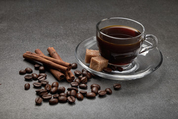 Naklejka premium glass Cup of coffee beans with cinnamon and sugar on a dark wooden background