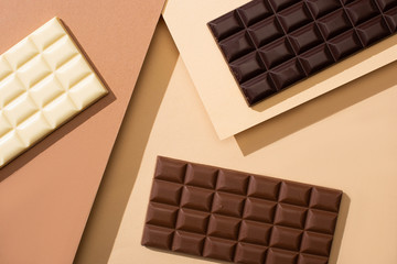 top view of delicious white, milk and dark chocolate bars on beige background