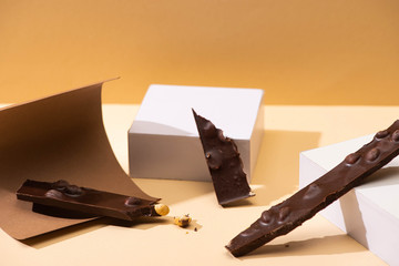 delicious dark chocolate with nuts pieces, paper and cubes on beige background